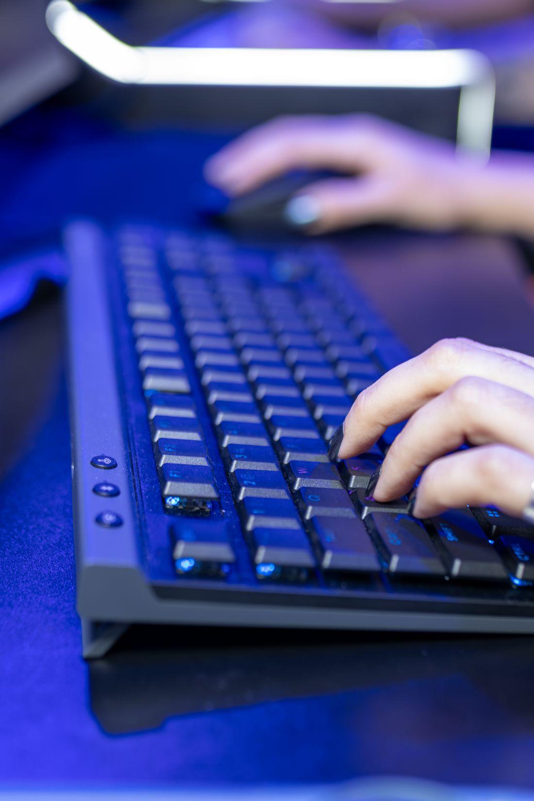 Tangan mengetik pada papan tombol laptop dengan cahaya biru redup