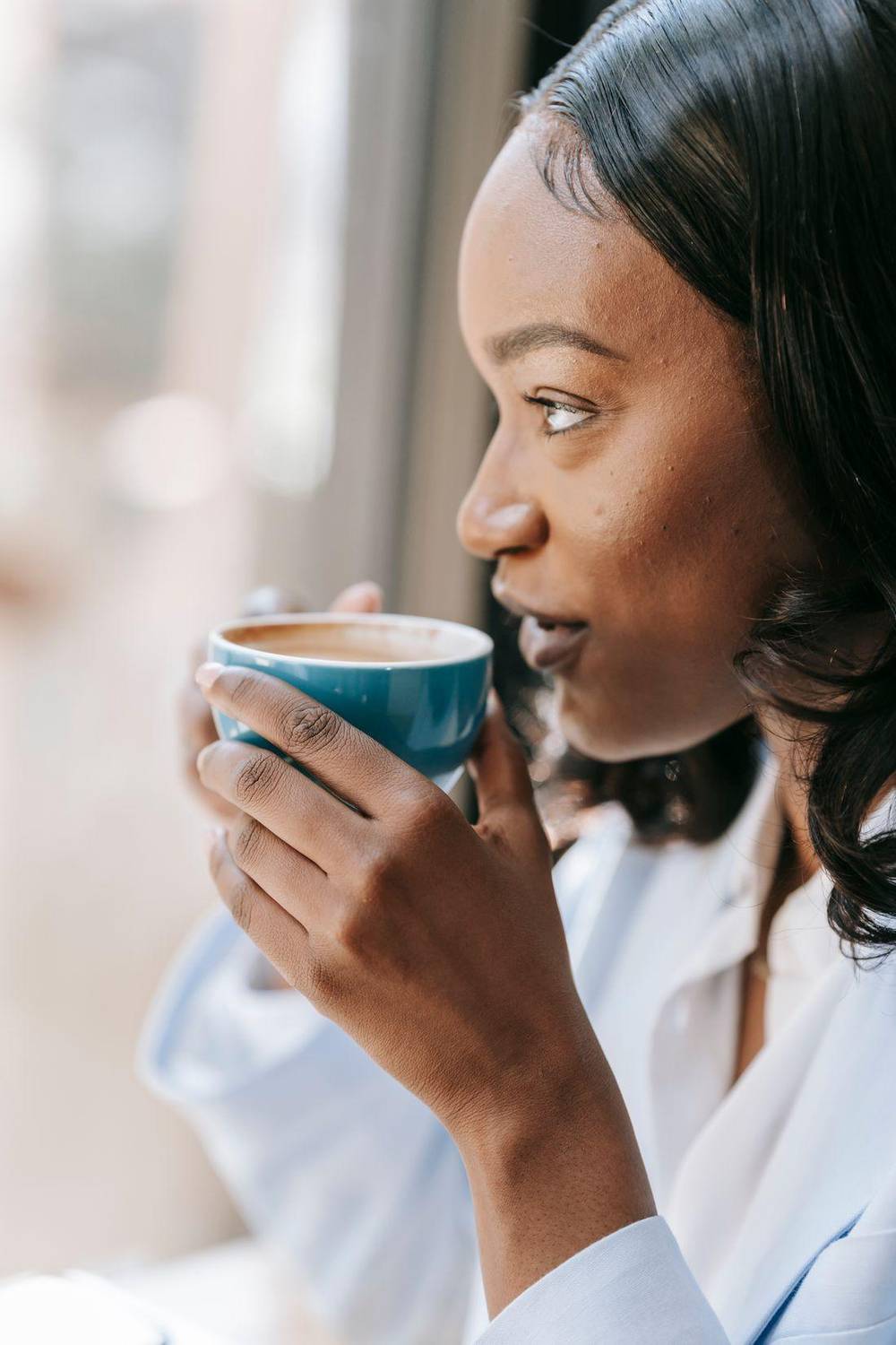 Perempuan menikmati kopi sambil memandang ke luar jendela dengan tenang