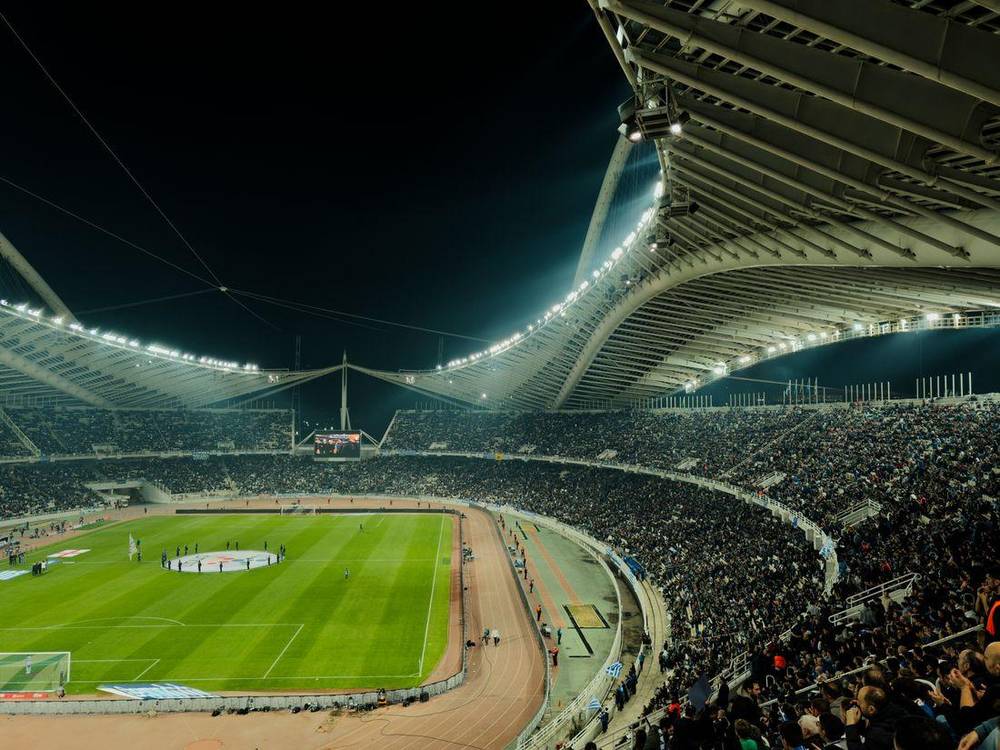 Stadion sepak bola malam hari dengan lampu sorot dan penonton memenuhi tribun